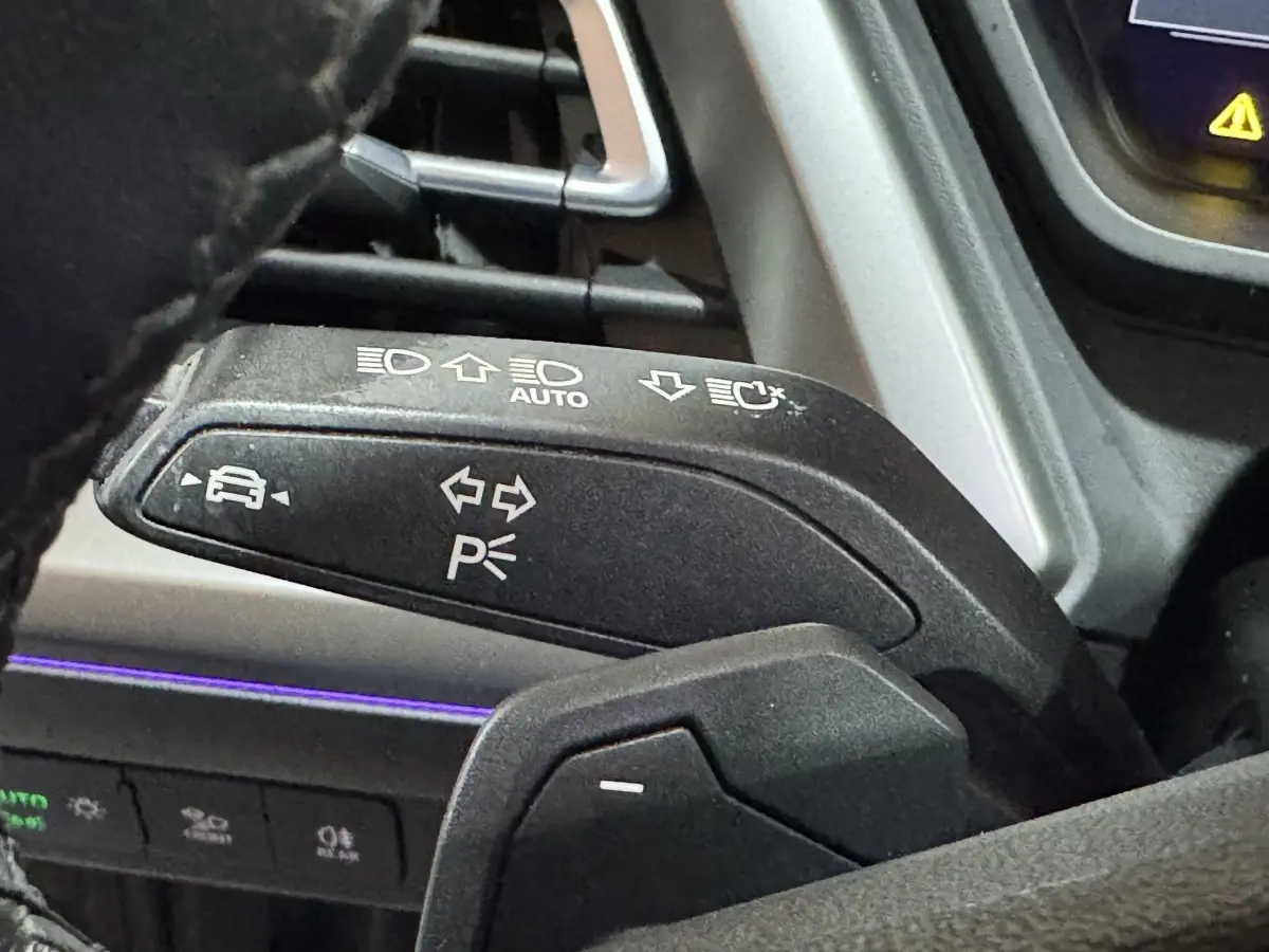Gros plan sur la commande de clignotants et feux, volant noir partiellement visible, intérieur gris foncé de l'Audi Q4 E-TRON.