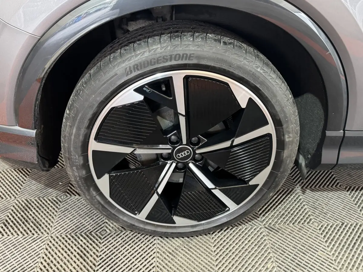 Gros plan sur la roue avant droite d’un Audi Q4 E-TRON gris foncé avec jante noire et argentée au design moderne.