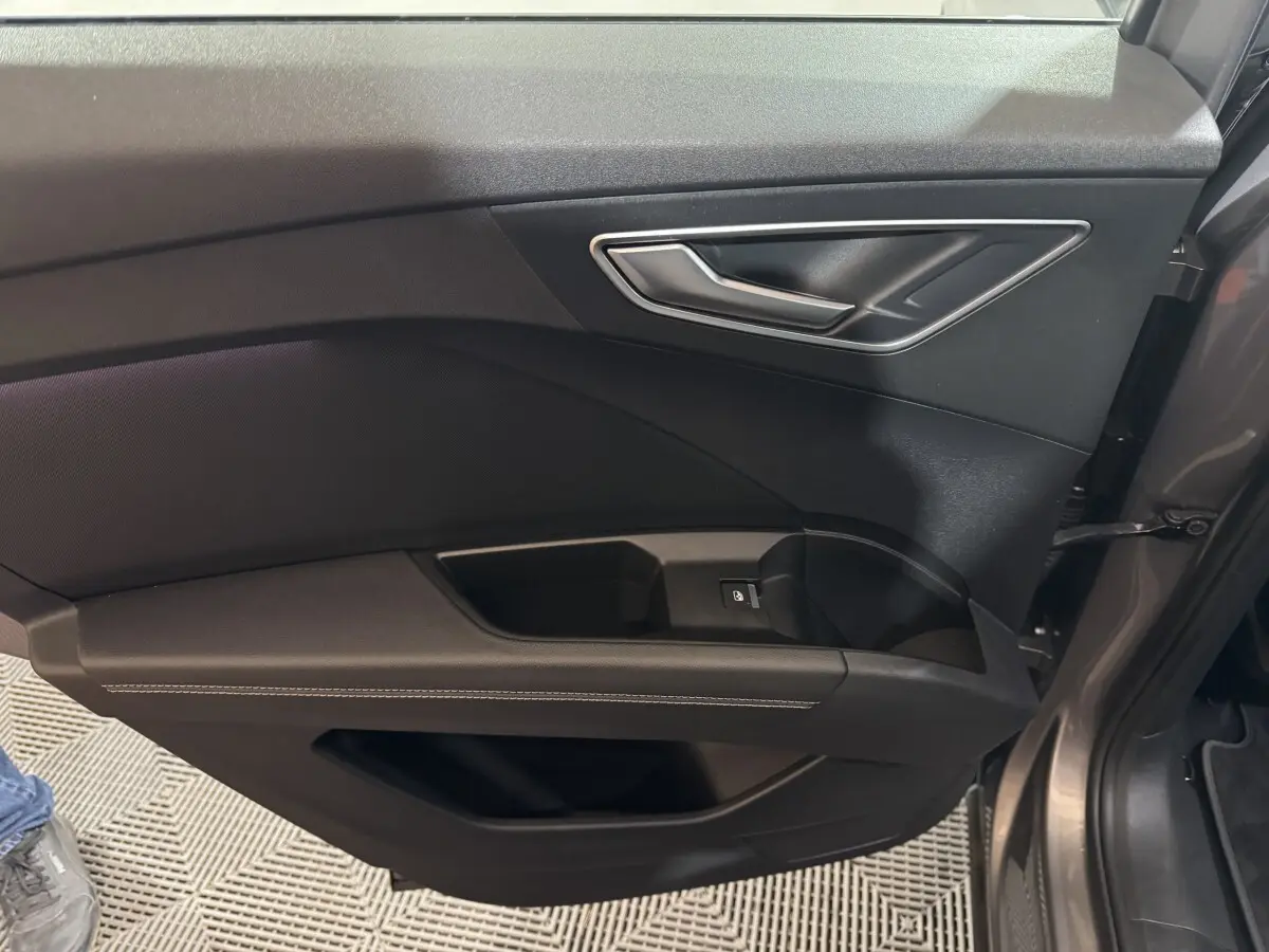 Vue rapprochée de la porte côté gauche gris foncé de l'Audi Q4 E-TRON avec poignée argentée et bouton de vitre électrique.