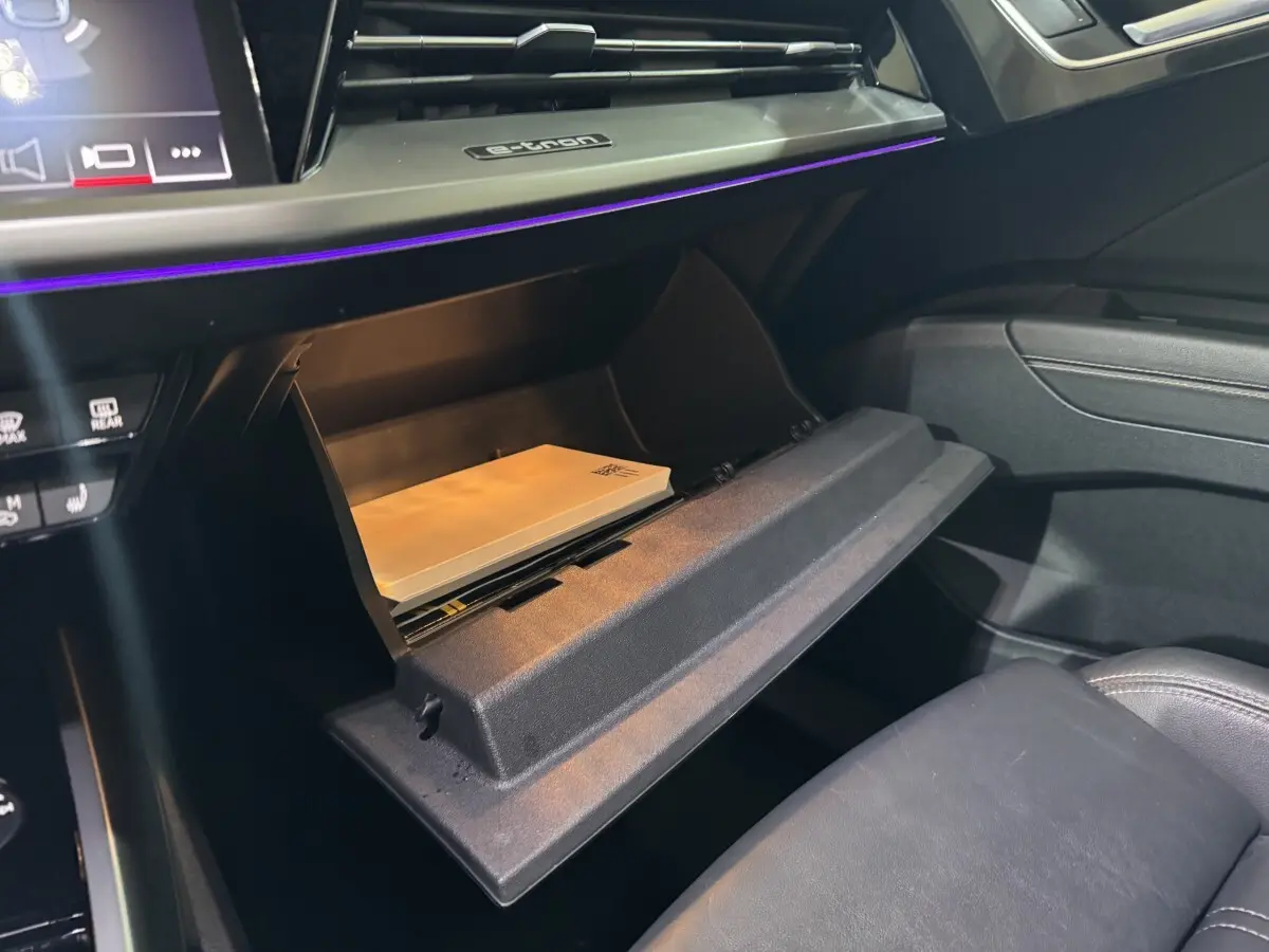 Gros plan sur la boîte à gants ouverte de l'Audi Q4 E-Tron gris foncé, avec éclairage d'ambiance violet visible.