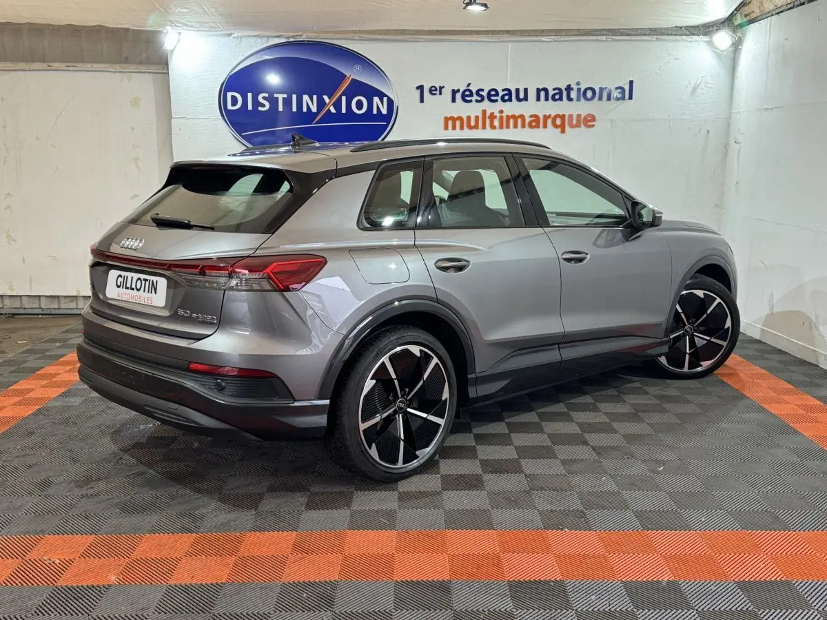 Audi Q4 E-TRON gris foncé en 3/4 arrière droit, avec jantes noires et toit panoramique visible en intérieur showroom.
