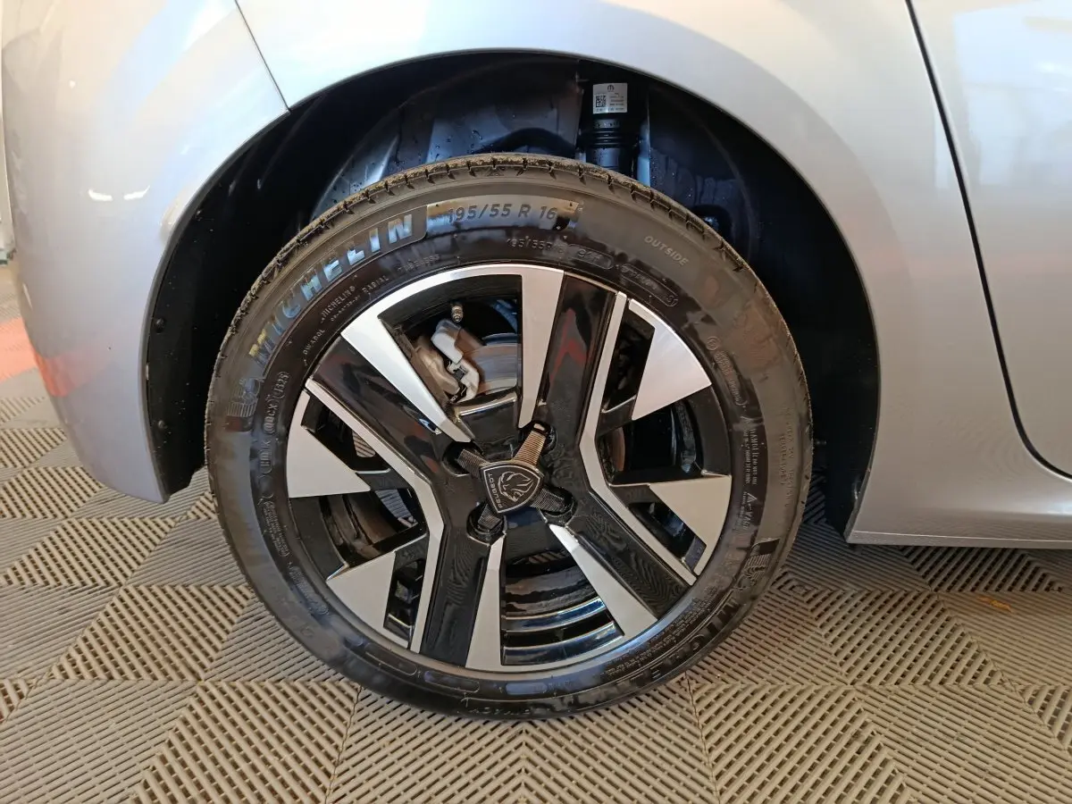 Gros plan sur la roue avant droite gris clair de la Peugeot 208 PureTech 100 S&S Allure avec jante noire et argentée.