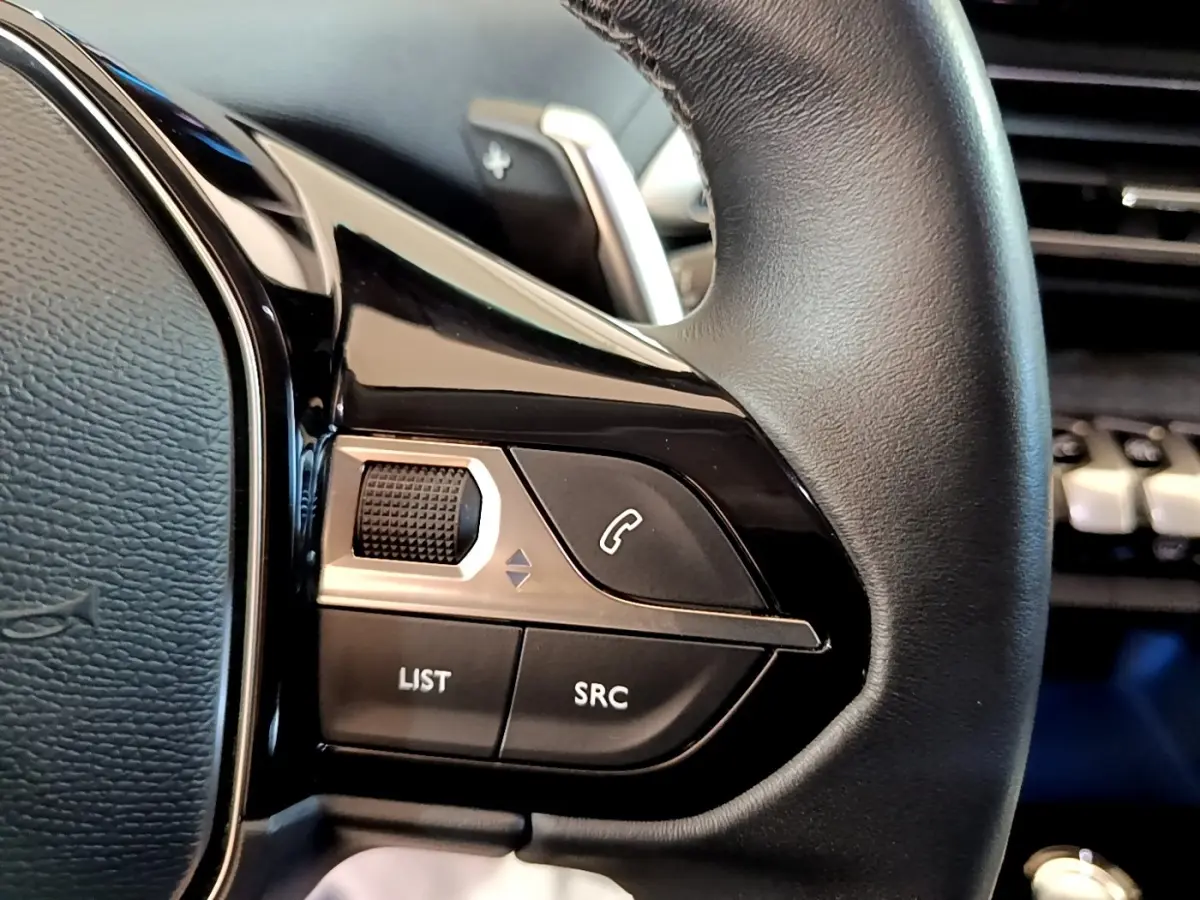 Gros plan sur les commandes gauche du volant cuir noir du Peugeot 3008 hybride, avec molette et boutons fonctionnels.