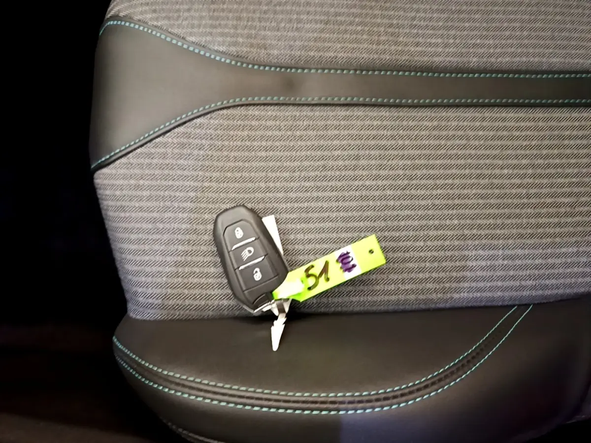Gros plan sur la clé de voiture posée sur un siège tissu gris et cuir noir avec surpiqûres bleues, intérieur Peugeot 3008 hybride.