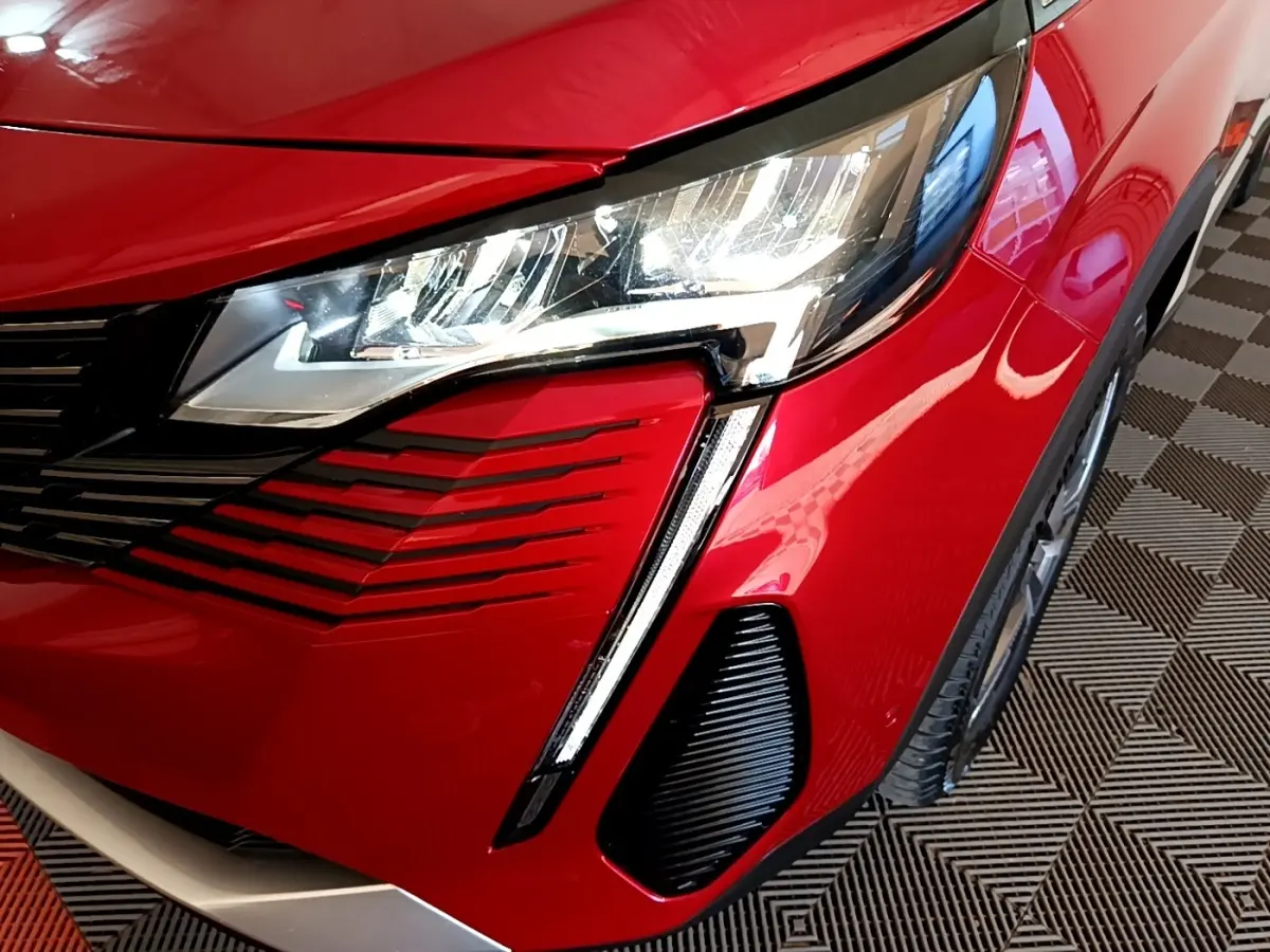 Gros plan sur l'avant droit rouge vif du Peugeot 3008 hybride, mettant en valeur le phare LED et la calandre noire.
