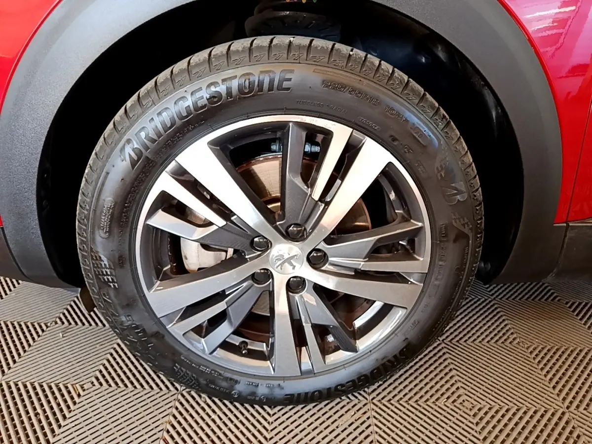 Gros plan sur la roue avant droite du Peugeot 3008 hybride rouge, avec jante alliage gris et pneu Bridgestone.