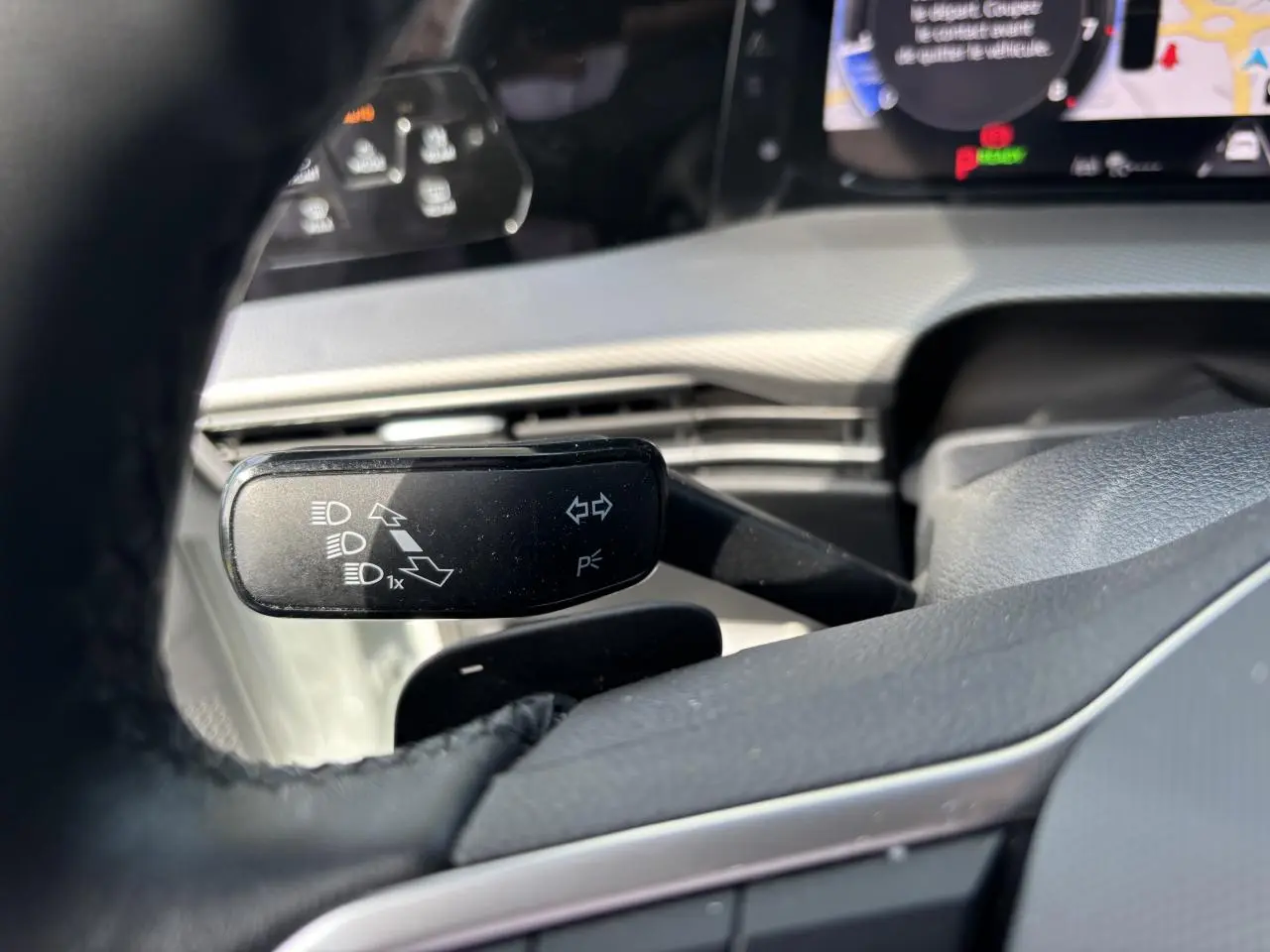 Détail du commodo gauche derrière le volant d’une Volkswagen Golf blanche 2024, avec tableau de bord numérique en arrière-plan.