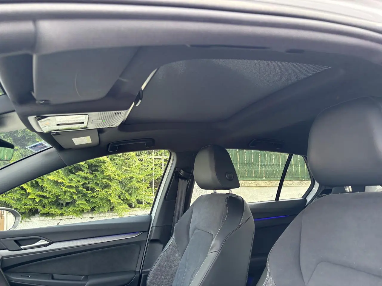 Vue intérieure côté conducteur de la Volkswagen Golf blanche 2024, mettant en valeur les sièges sport et le toit noir.