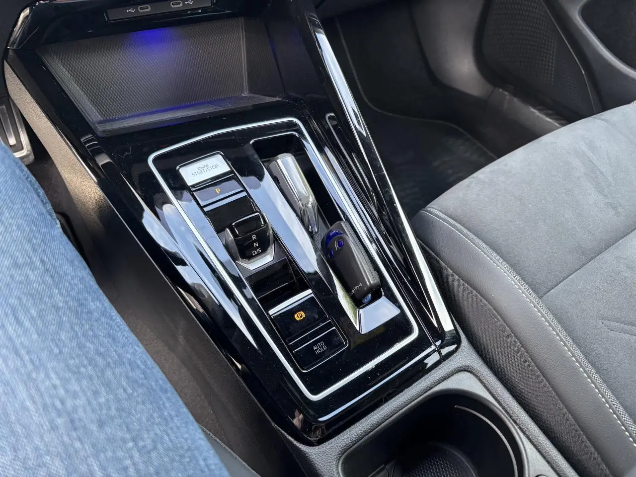 Gros plan sur la console centrale noire brillante de la Volkswagen Golf blanche 2024, avec levier de boîte auto et bouton start/stop.