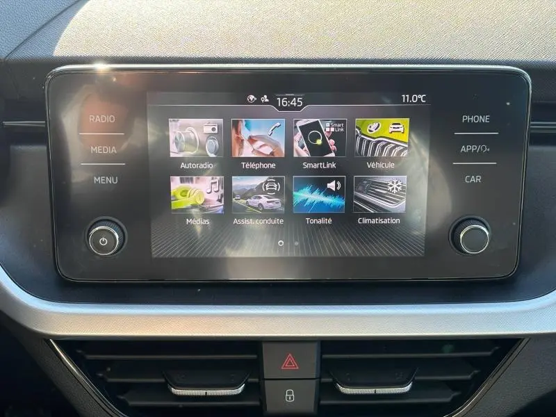 Écran tactile central du Skoda Kamiq 2023 affichant les menus multimédia et assistance à la conduite, entouré de commandes.