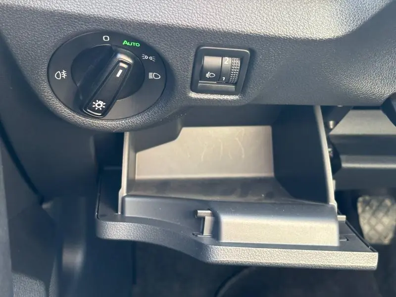 Gros plan sur le compartiment de rangement ouvert et les commandes d'éclairage du tableau de bord d'un Skoda Kamiq noir Magic nacré.