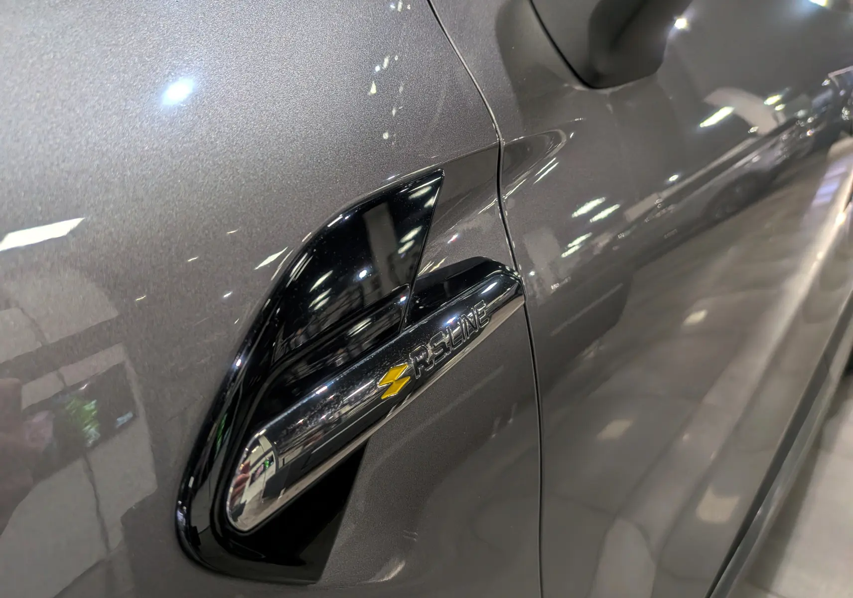 Gros plan sur l'aile avant gauche gris Cassiopé du Renault Captur R.S. Line avec logo distinctif jaune et noir.