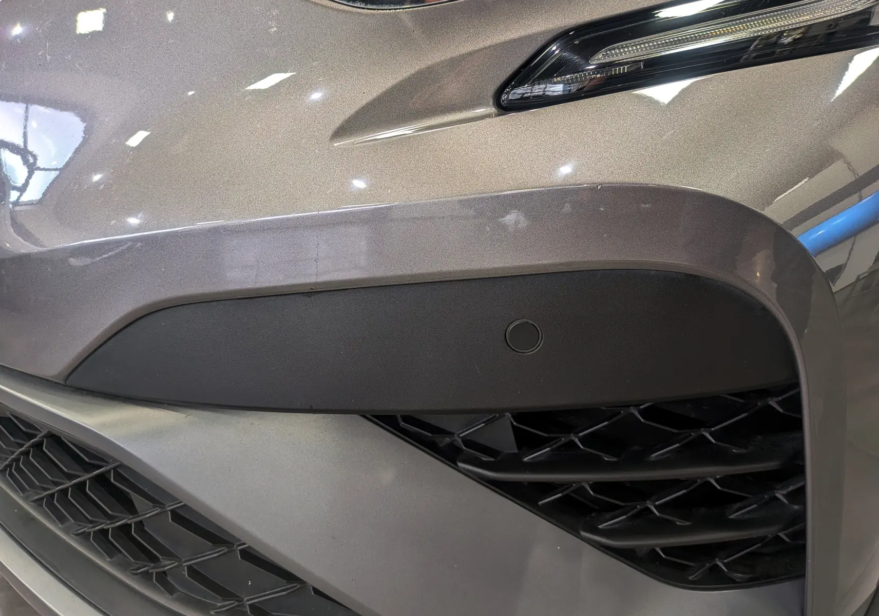 Gros plan sur l'avant droit gris Cassiopé du Renault Captur 2022, mettant en valeur la calandre et le capteur de stationnement.