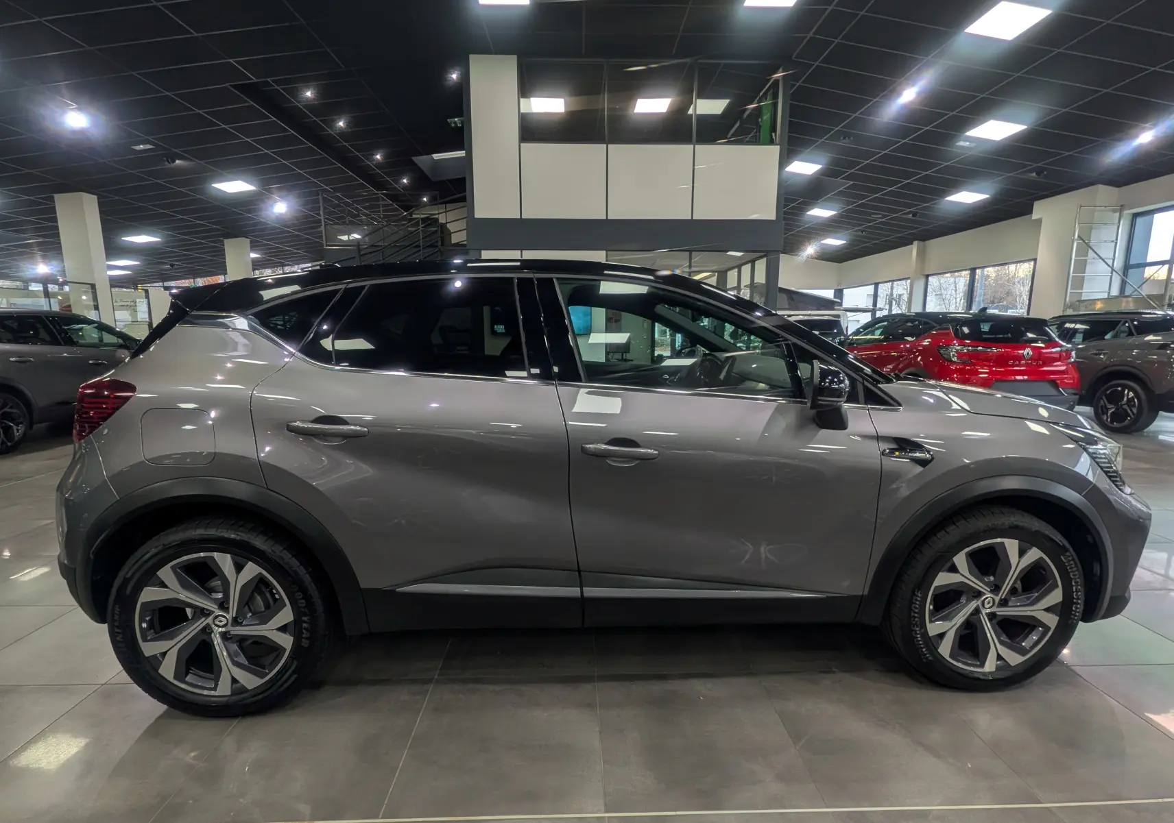 Profil droit d'un Renault Captur TCe 160 R.S. Line 2022 gris Cassiopé avec toit noir en showroom lumineux.
