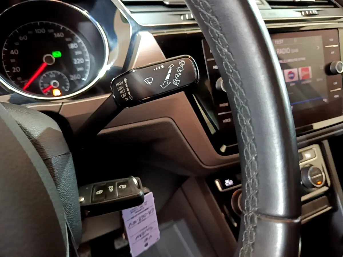 Gros plan sur le volant cuir et la commande d'essuie-glace du Volkswagen Touran 1.5 TSI bleu, tableau de bord et écran tactile visibles.