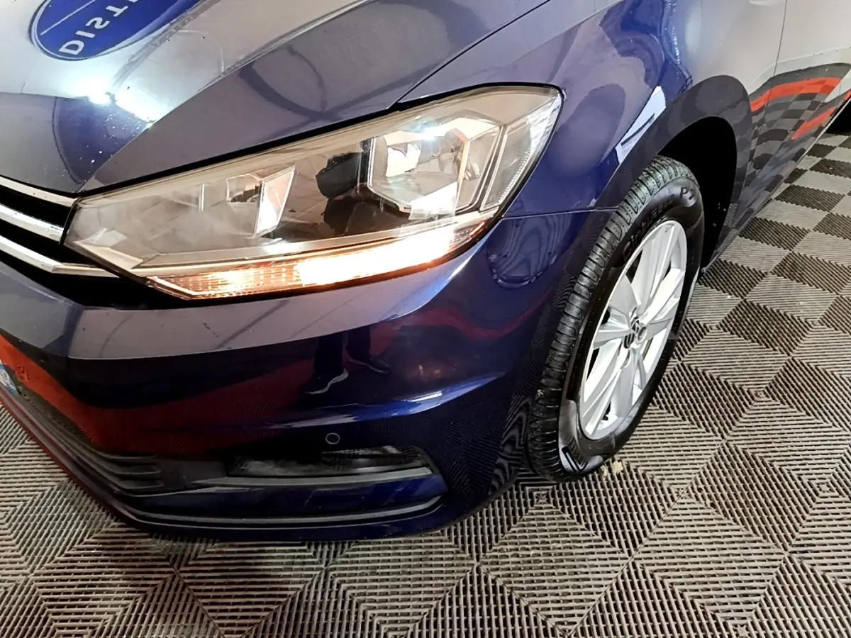 Gros plan sur l'avant droit bleu d'un Volkswagen Touran 1.5 TSI EVO DSG7 avec phare allumé et jante alliage.