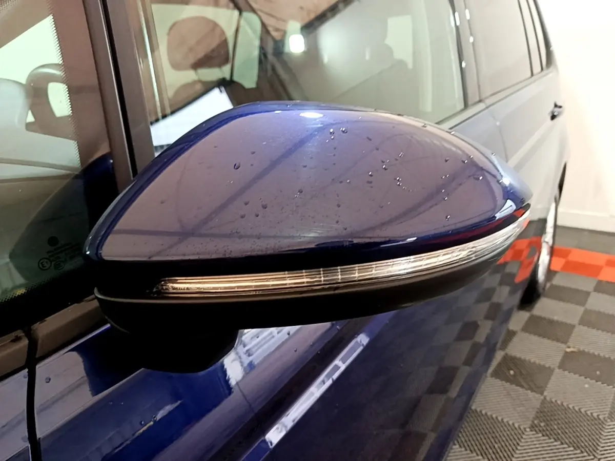 Rétroviseur côté gauche bleu du Volkswagen Touran 2021 avec clignotant intégré, vue rapprochée en intérieur.