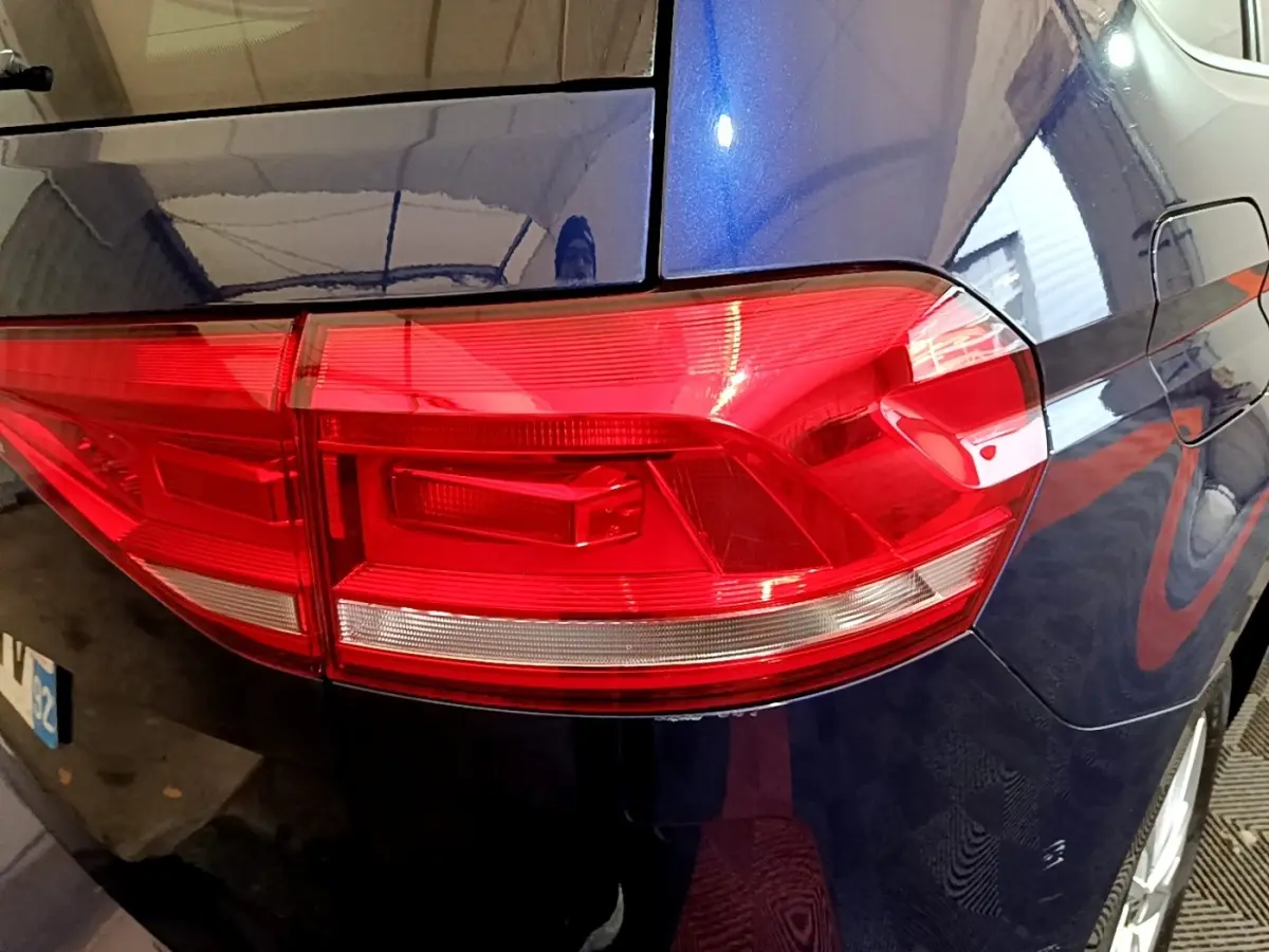 Gros plan sur le feu arrière gauche rouge d’un Volkswagen Touran bleu 2021, avec reflet intérieur visible.