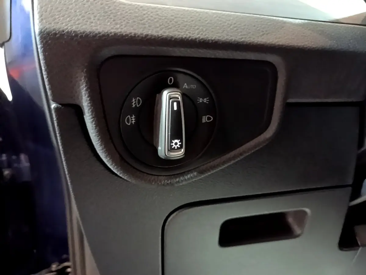 Gros plan sur le sélecteur des phares noir dans l'habitacle du Volkswagen Touran bleu, côté gauche conducteur.