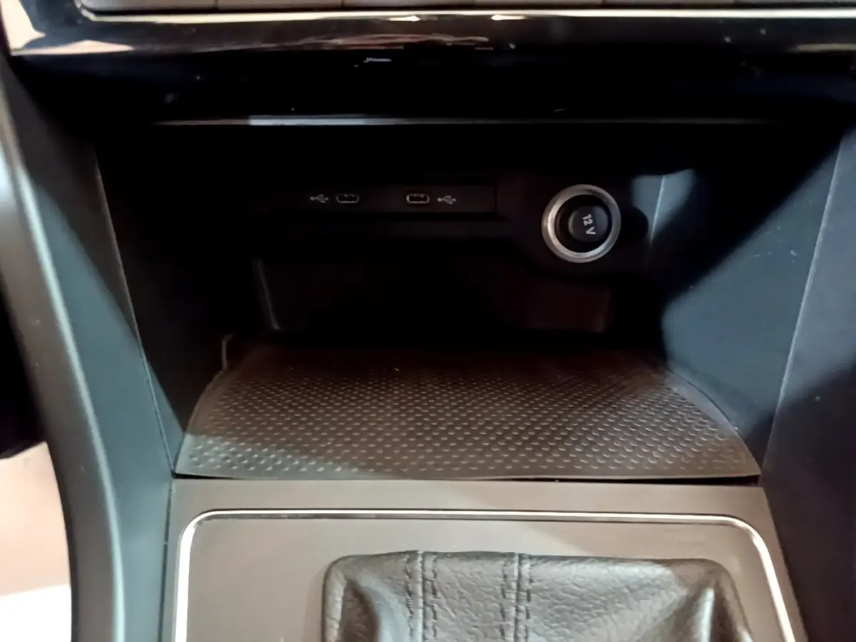 Gros plan sur la console centrale noire du Volkswagen Touran 1.5 TSI EVO DSG7 avec prise 12V et ports USB visibles.