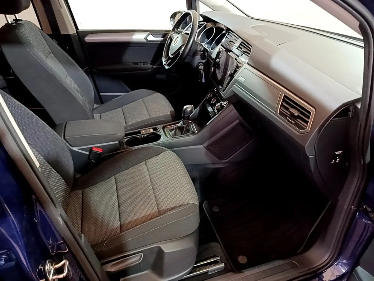 Intérieur avant du Volkswagen Touran bleu 2021, vue côté conducteur, tableau de bord moderne avec écran tactile central.