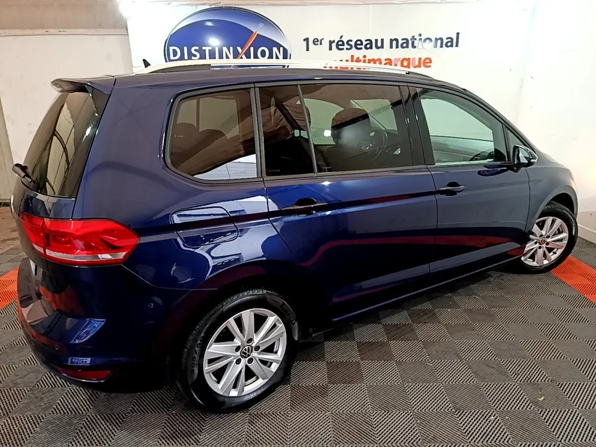 Vue côté droit arrière d'un Volkswagen Touran bleu 2021 garé en intérieur sur sol damier noir et rouge.