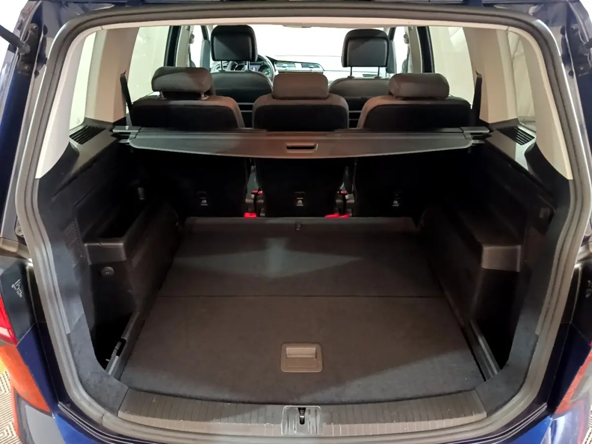 Vue arrière du coffre ouvert du Volkswagen Touran bleu 1.5 TSI EVO DSG7 United avec banquette arrière et cache-bagages visibles.