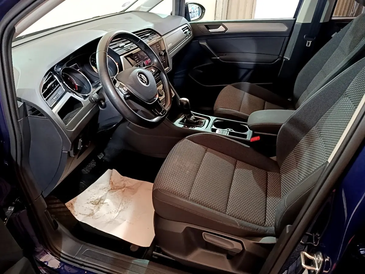 Vue intérieure côté conducteur du Volkswagen Touran bleu 2021, montrant le volant cuir multifonctions et les sièges tissu gris.