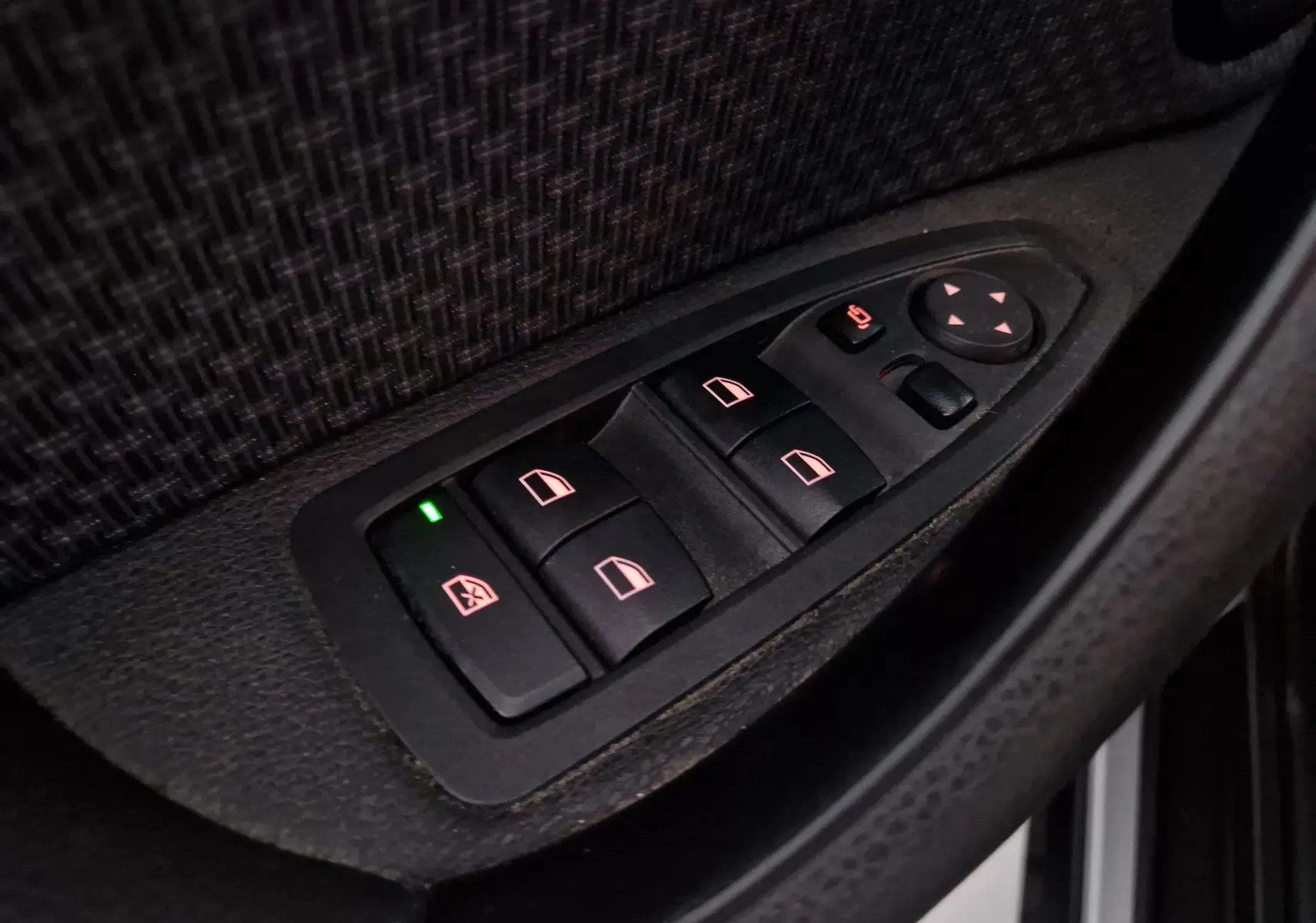 Gros plan sur les commandes de lève-vitres et rétroviseurs côté gauche d'une BMW X2 gris clair métal de 2018.