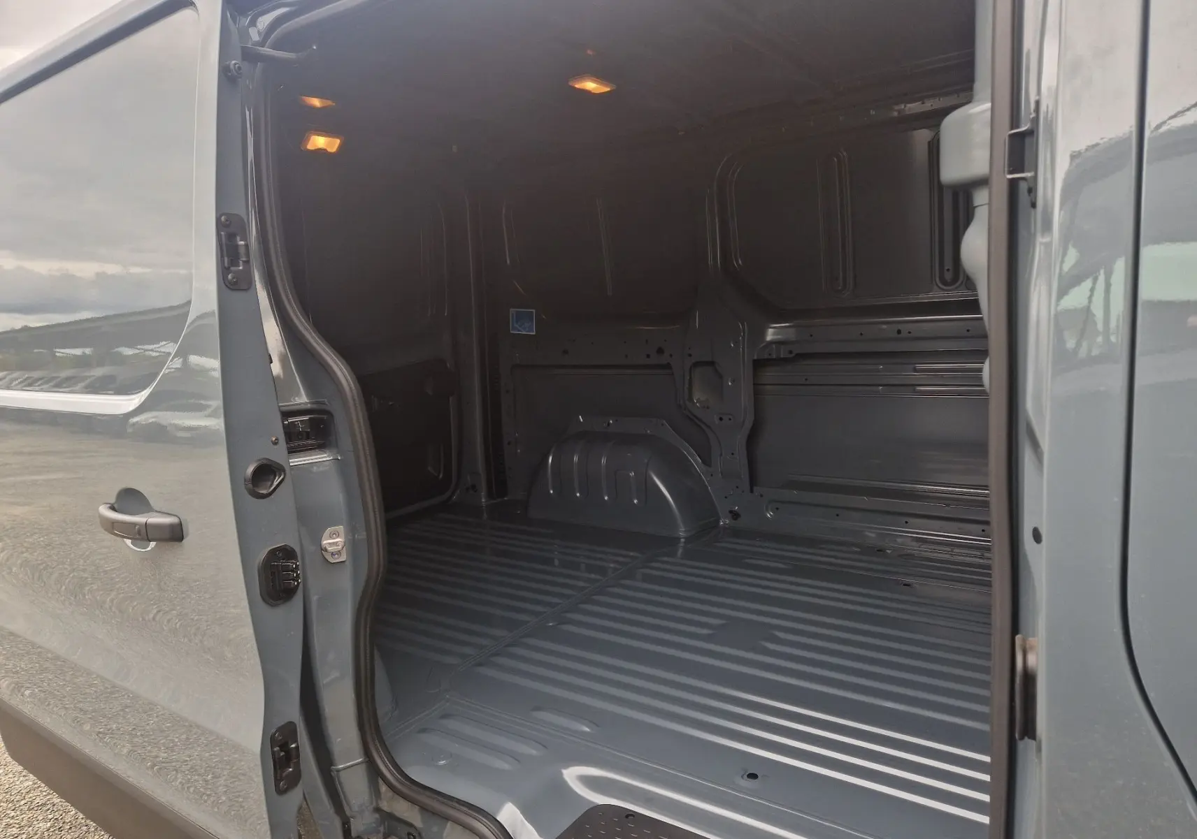 Vue intérieure arrière du Renault Trafic Fourgon gris Highland, montrant l’espace de chargement vide et éclairé.