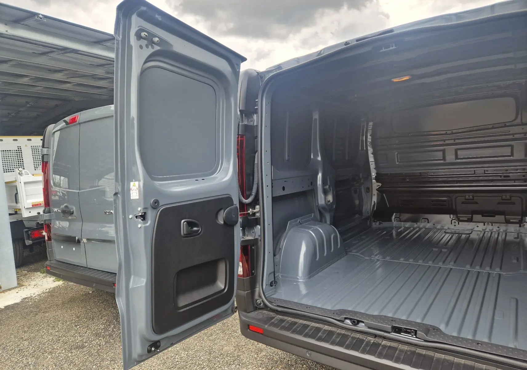 Vue arrière droite du Renault Trafic Fourgon gris Highland 2025 avec portes ouvertes et intérieur de chargement vide.