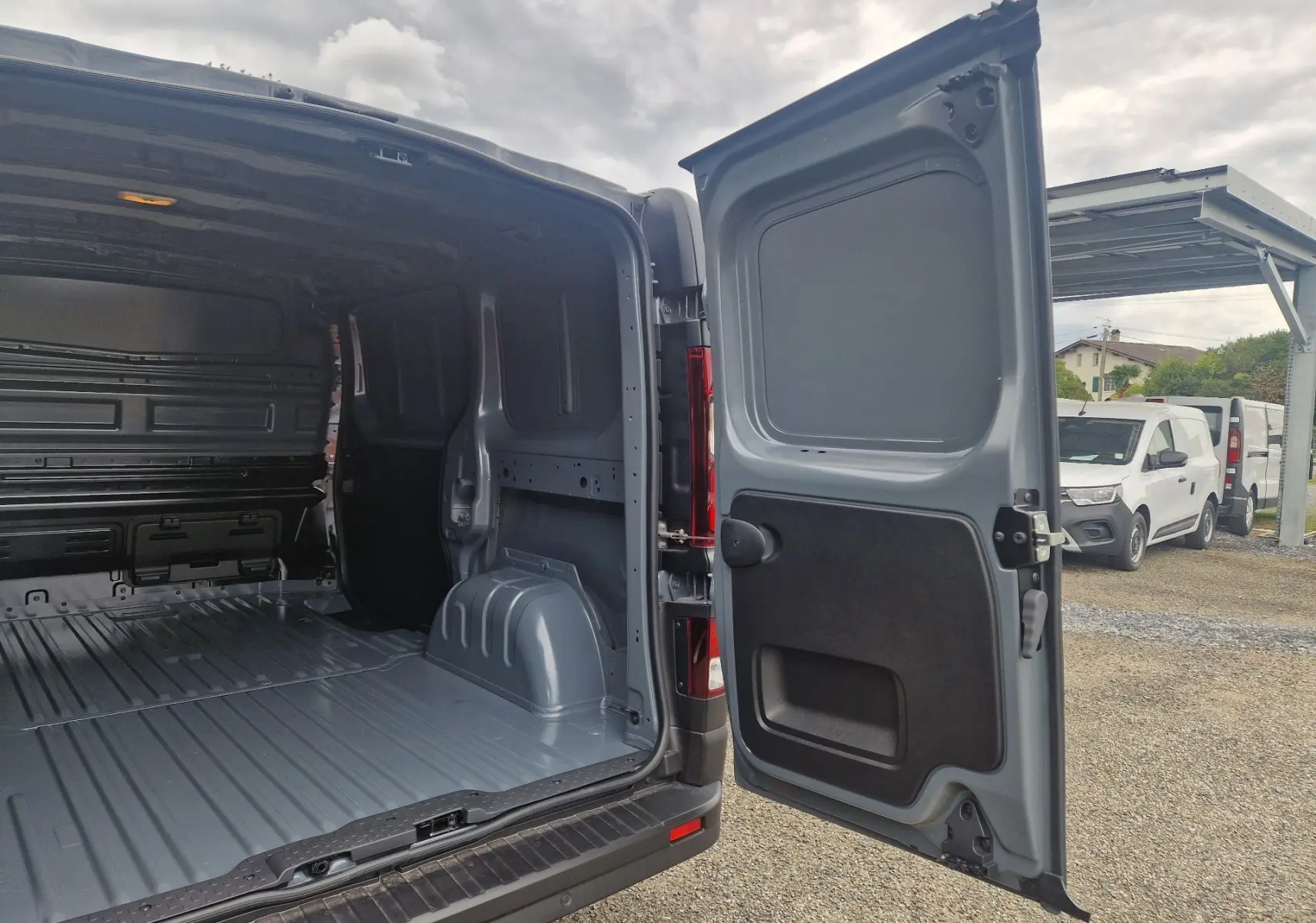 Vue arrière ouverte du Renault Trafic Fourgon gris Highland montrant l’espace de chargement vide et la porte battante droite.