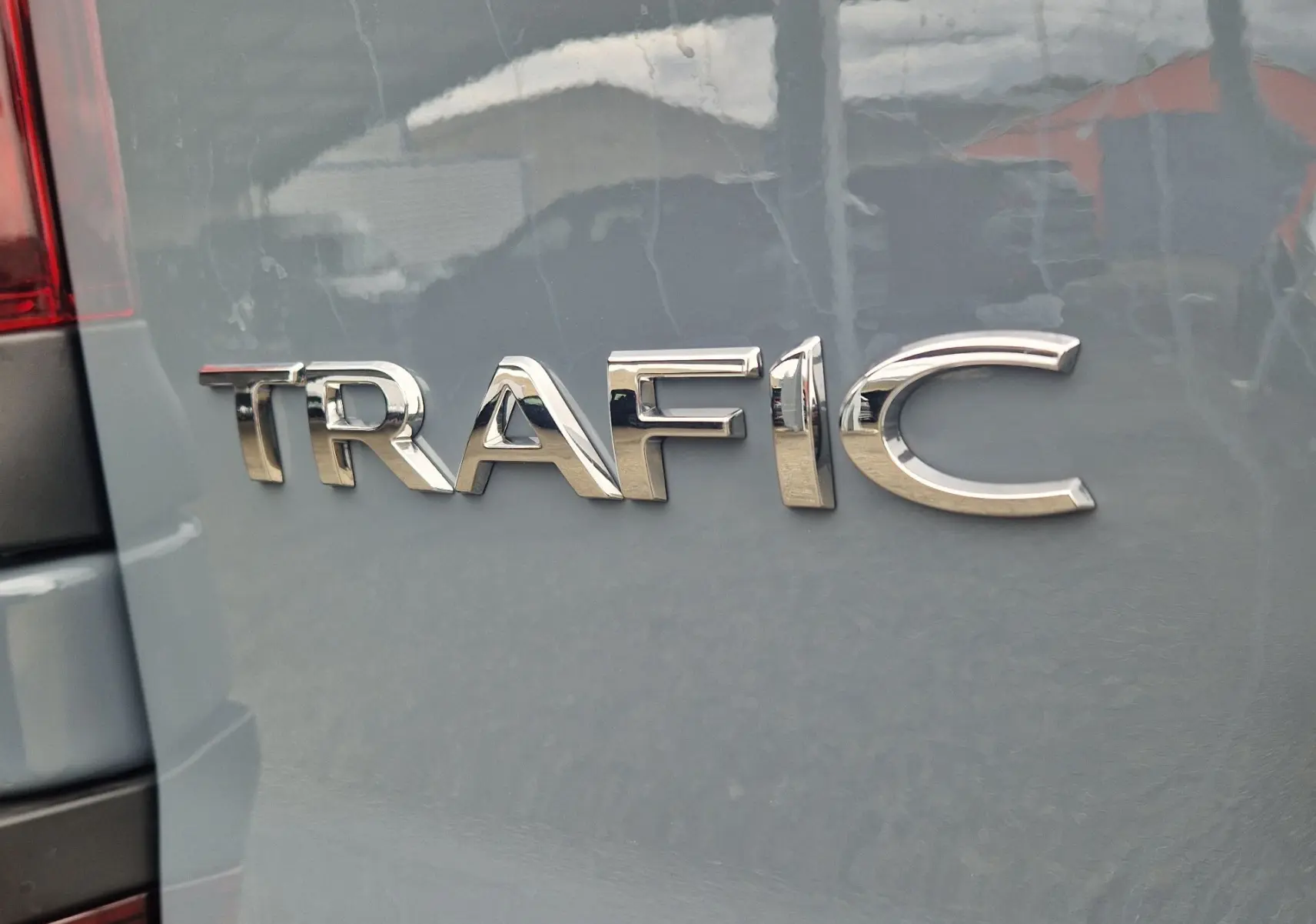 Gros plan sur l’inscription TRAFIC en chrome sur la porte arrière d’un Renault Trafic gris Highland.