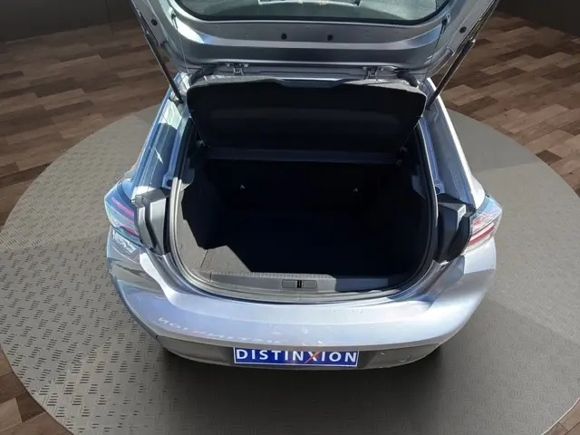 Vue arrière en plongée d'une Peugeot 208 gris clair 2025 avec coffre ouvert et intérieur de coffre visible.