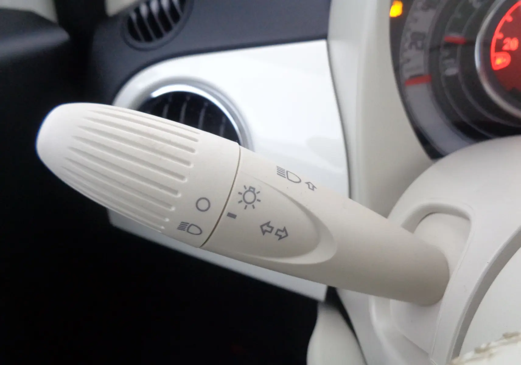 Gros plan sur la manette de clignotants beige dans l'habitacle blanc gelato d'une Fiat 500 hybride 2023.