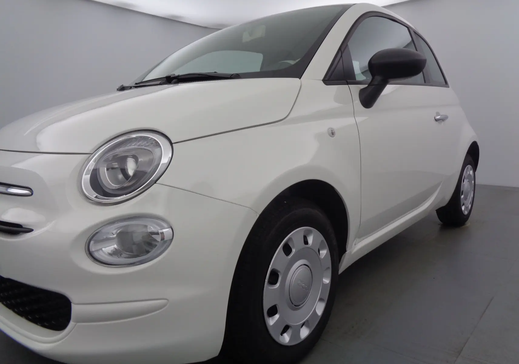 Fiat 500 blanc gelato vue 3/4 avant droit, mettant en valeur ses phares ronds et ses jantes acier classiques.