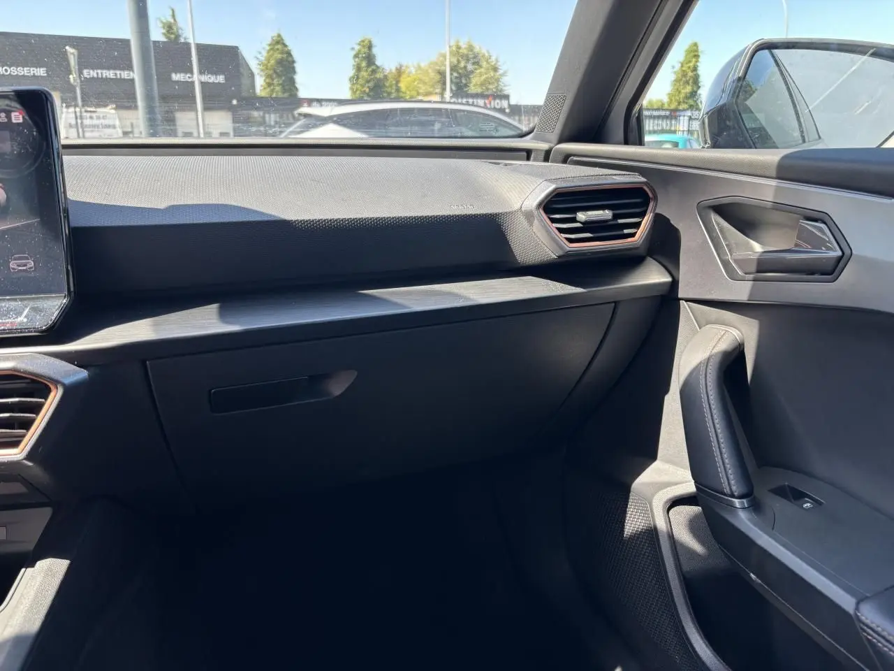 Vue intérieure côté passager du tableau de bord et de la portière d'une CUPRA Leon Sportstourer 2024 avec finitions noires et inserts cuivrés.