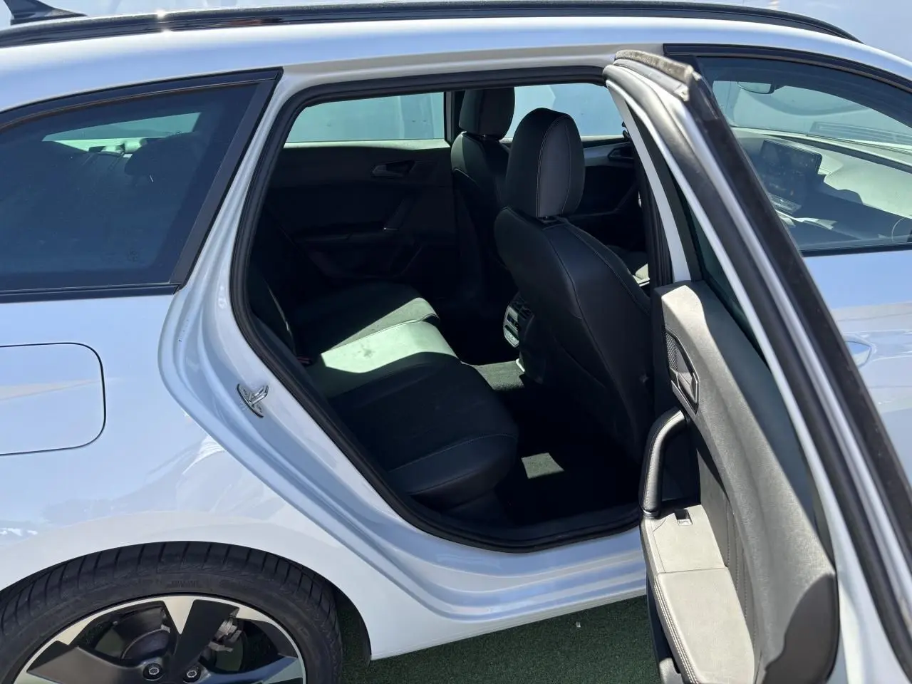 Vue côté gauche arrière d'une CUPRA Leon Sportstourer blanc Nevada, porte ouverte révélant l'intérieur noir et les jantes alliage 18 pouces.