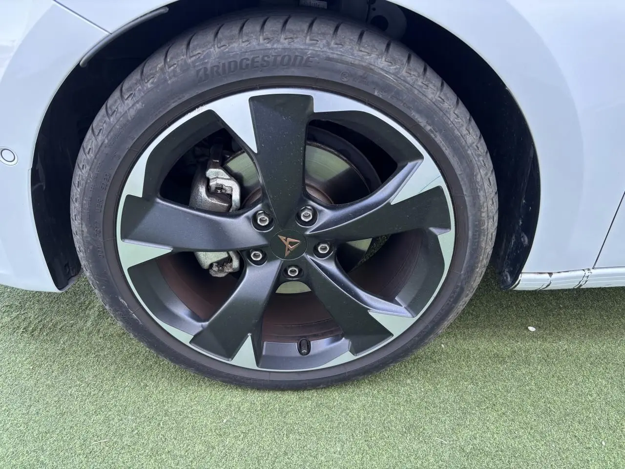 Gros plan sur la jante avant droite noire et argentée avec logo CUPRA sur une carrosserie blanc Nevada.