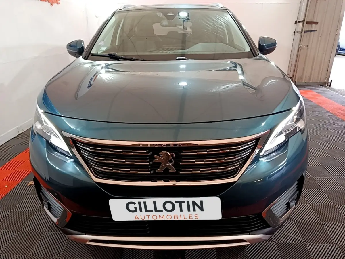 Vue avant d'un Peugeot 5008 bleu métallisé avec calandre chromée et phares LED allumés dans un garage.