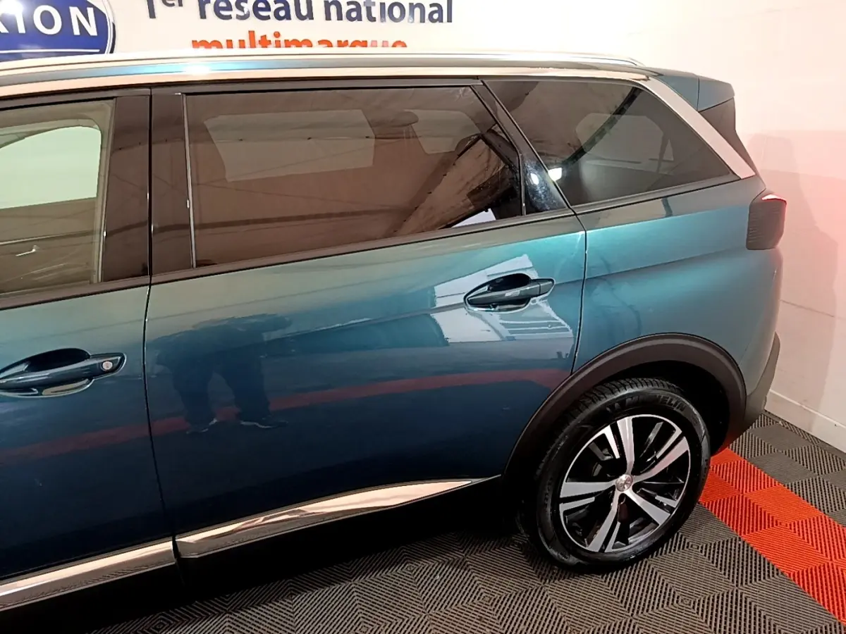 Vue latérale droite du Peugeot 5008 bleu 2018 avec jantes alliage et vitres teintées dans un showroom.