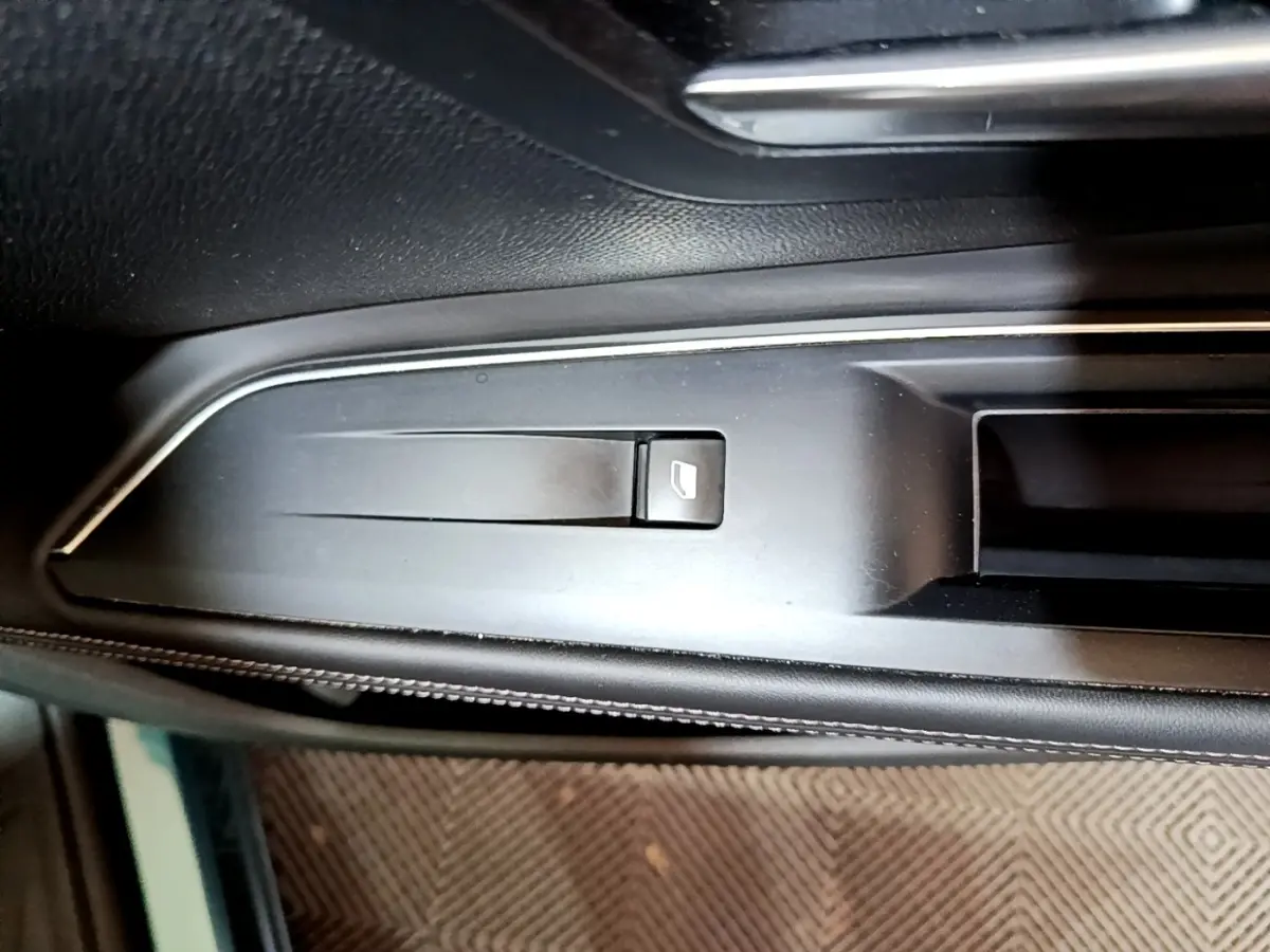 Gros plan sur la commande de lève-vitre côté gauche dans l'habitacle noir du Peugeot 5008 bleu 2018.