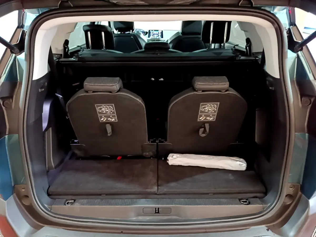 Vue arrière du coffre ouvert d'un Peugeot 5008 bleu, montrant la 3ème rangée de sièges individuels et l'intérieur sombre.