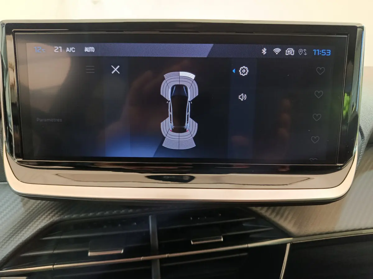 Écran tactile central affichant l'aide au stationnement avec vue aérienne du véhicule dans un Peugeot 208 gris clair.