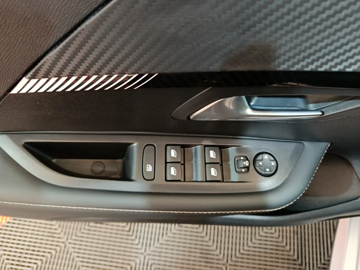 Vue rapprochée de la commande des vitres et rétroviseurs côté gauche dans l’habitacle d’une Peugeot 208 gris clair.