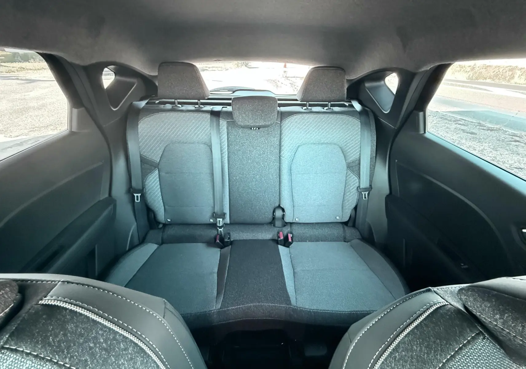 Vue intérieure arrière du Renault Captur 2025, sièges tissu gris noir avec ceintures de sécurité visibles.