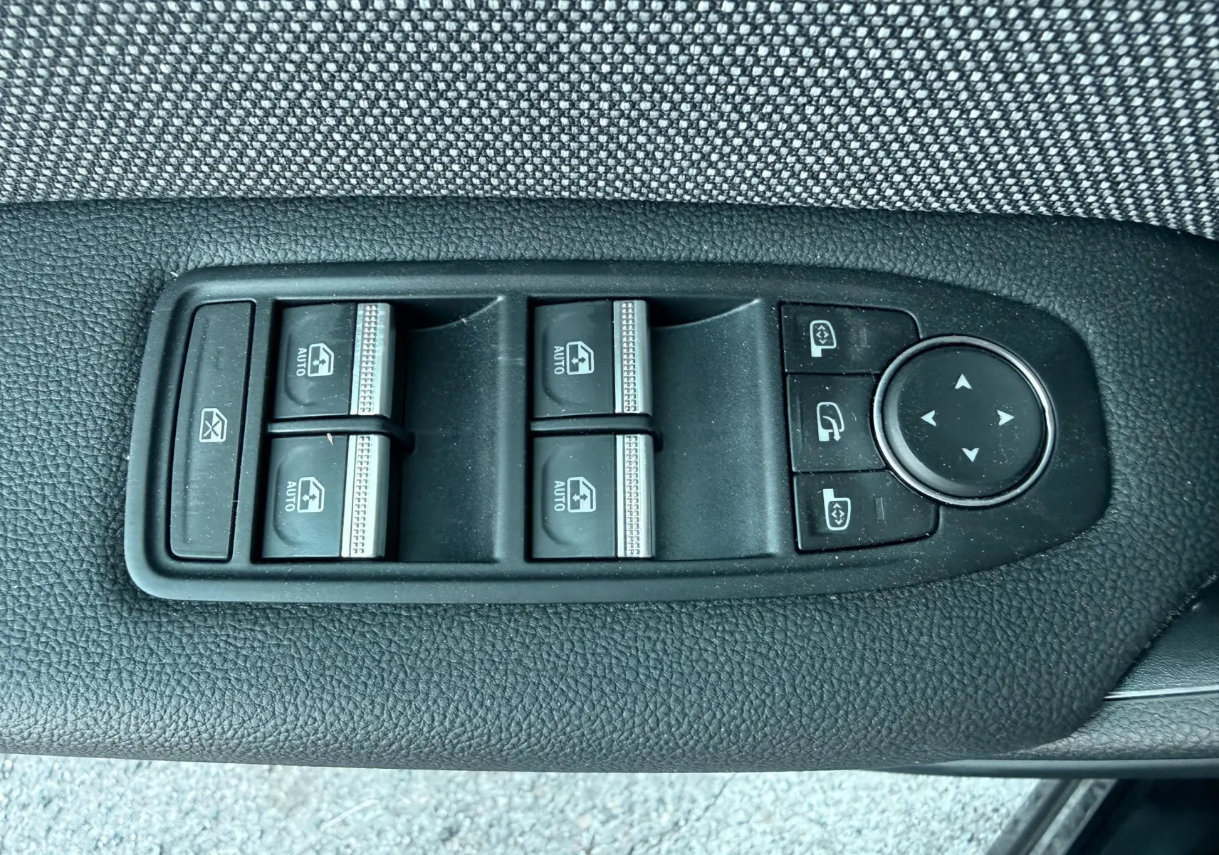 Gros plan sur les commandes des vitres électriques et des rétroviseurs sur la porte côté gauche d’un Renault Captur noir.