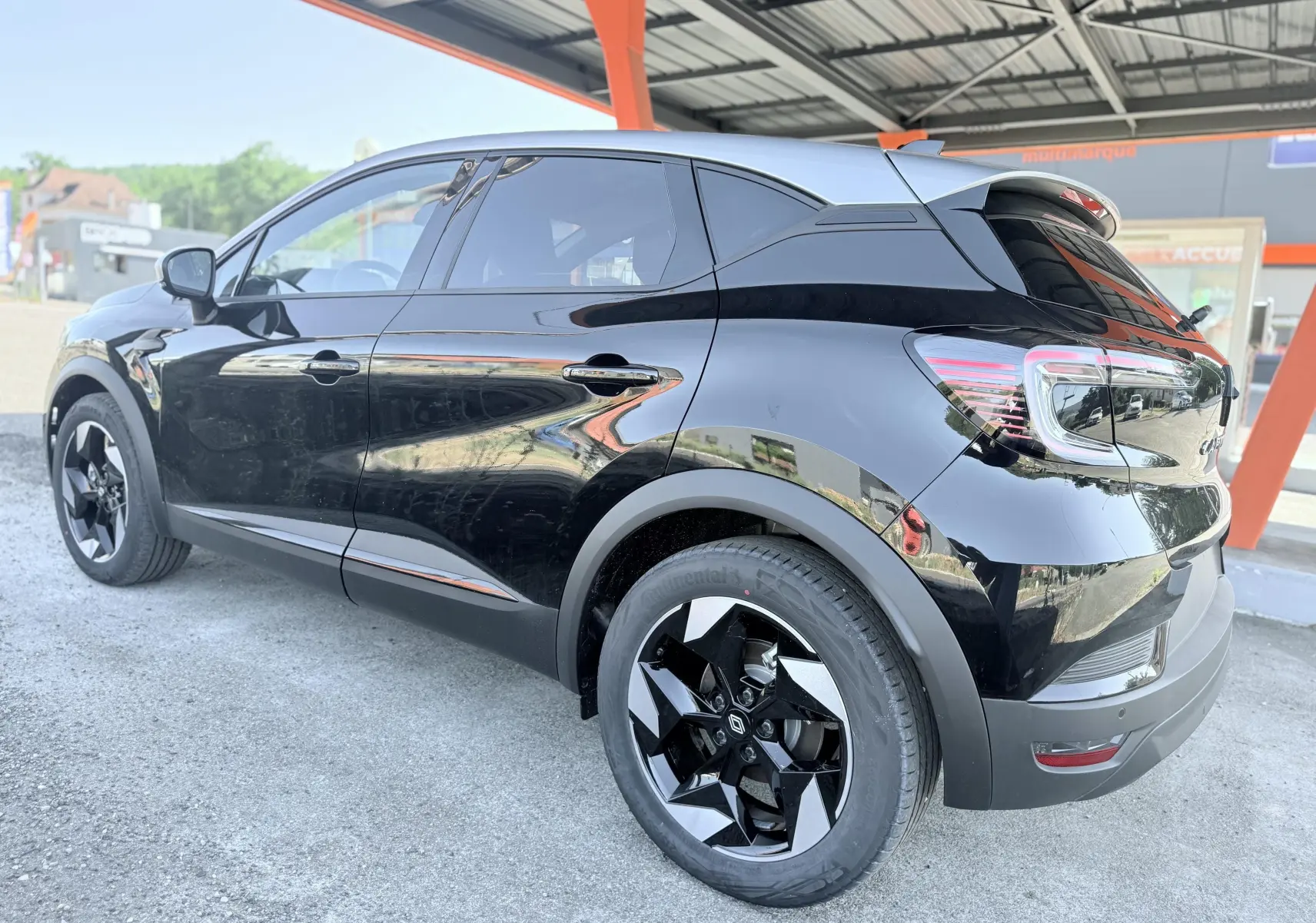 Vue 3/4 arrière droite d'un Renault Captur noir brillant avec jantes bicolores et vitres teintées.
