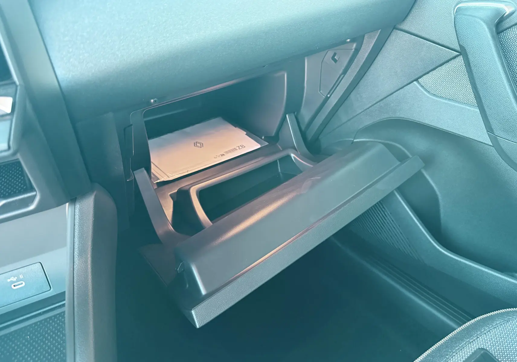 Gros plan sur la boîte à gants ouverte côté passager du Renault Captur noir, montrant des documents à l'intérieur.