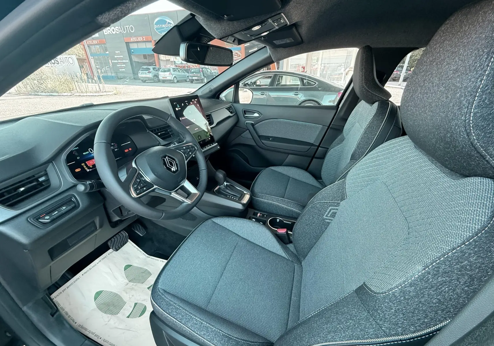Vue intérieure côté conducteur du Renault Captur 2025, sièges tissu gris noir et tableau de bord moderne.